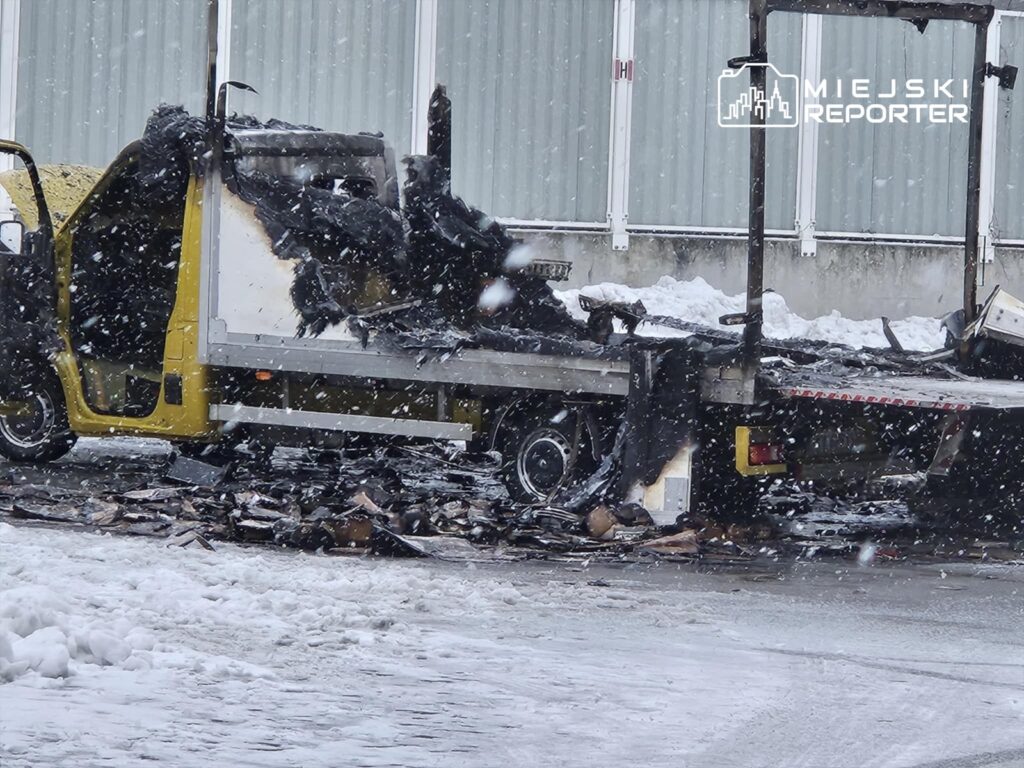 Zniszczona żółta ciężarówka z poparzoną kabiną stoi na zaśnieżonej drodze, otoczona resztkami spalonego ładunku.
