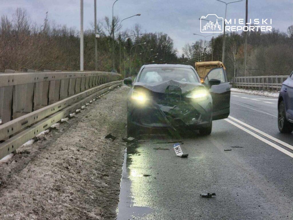 Zniszczony samochód osobowy stoi na drodze, obok leży odłamany element karoserii.