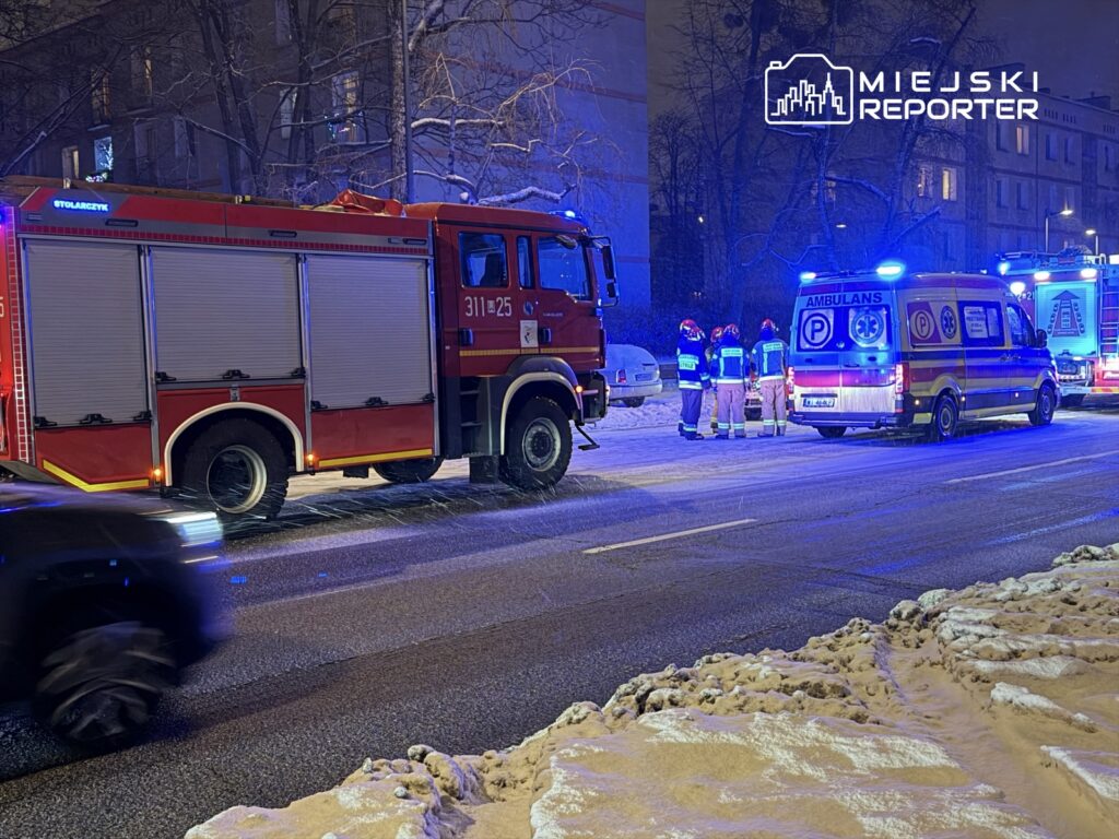 Czerwony wóz strażacki i ambulans zatrzymane na ośnieżonej ulicy, z ratownikami omawiającymi sytuację.