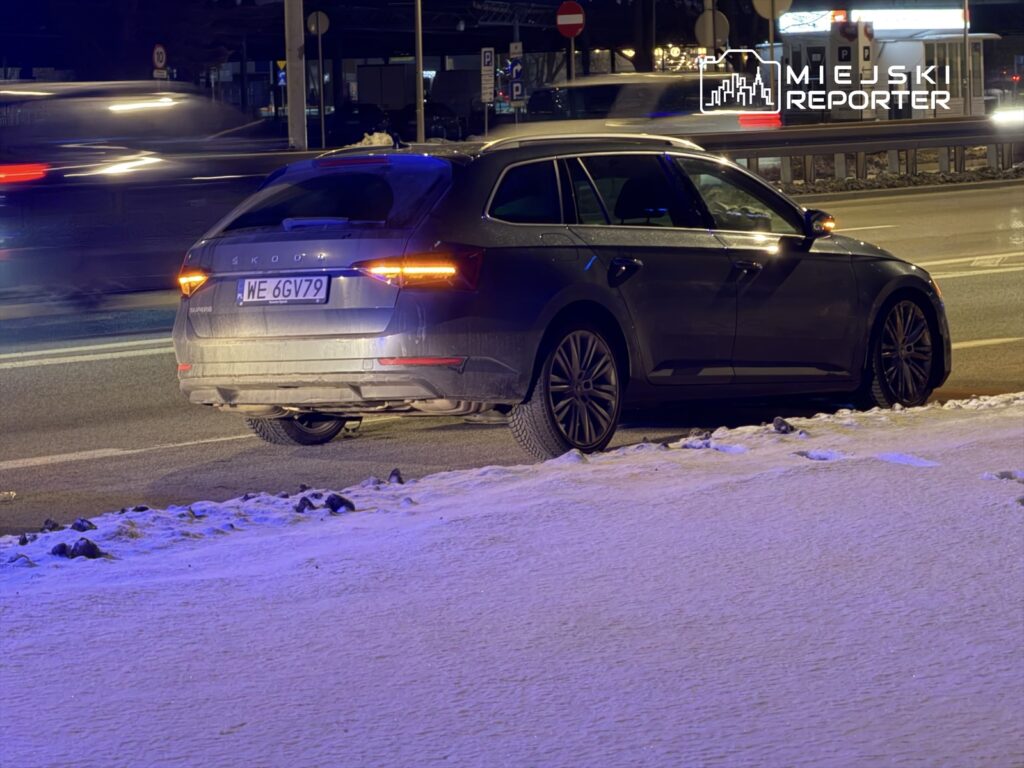 Czarny samochód osobowy marki Skoda zaparkowany na poboczu drogi, obok ośnieżonego terenu.