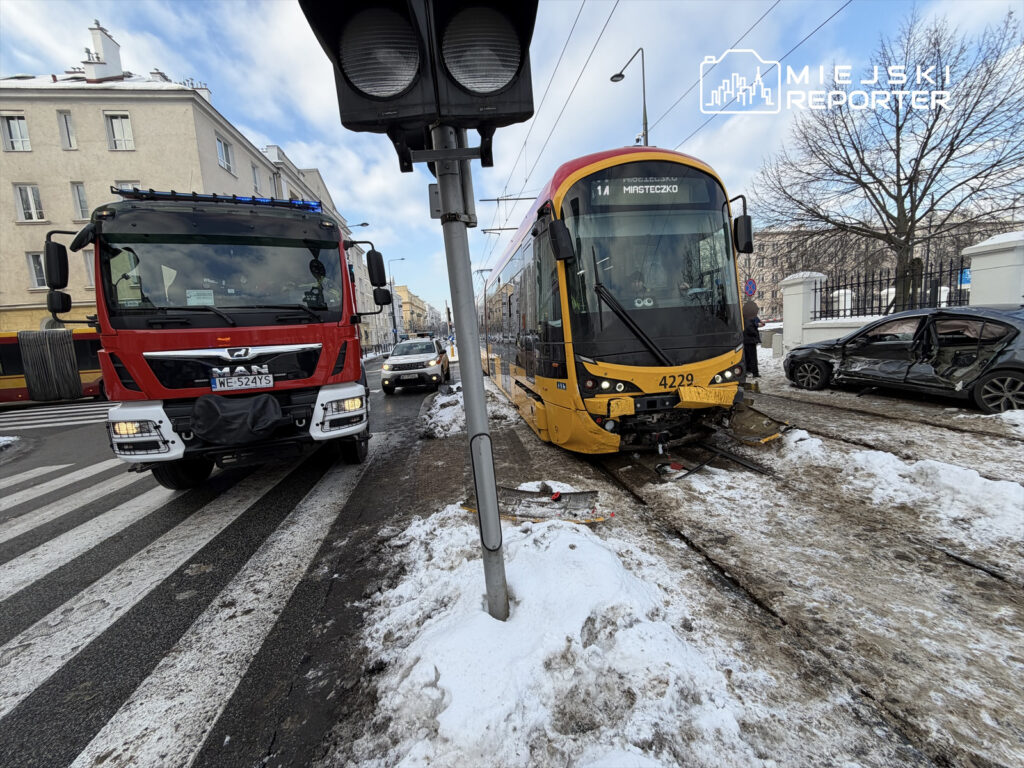 Czerwony wóz strażacki zatrzymany na przejściu dla pieszych obok uszkodzonego tramwaju i samochodu osobowego w zimowej scenerii.