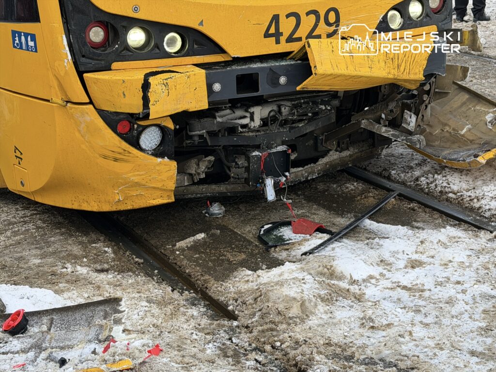 Uszkodzony żółty tramwaj z wgniecionym przodem stoi na torach, otoczony śniegiem i fragmentami zderzaka.