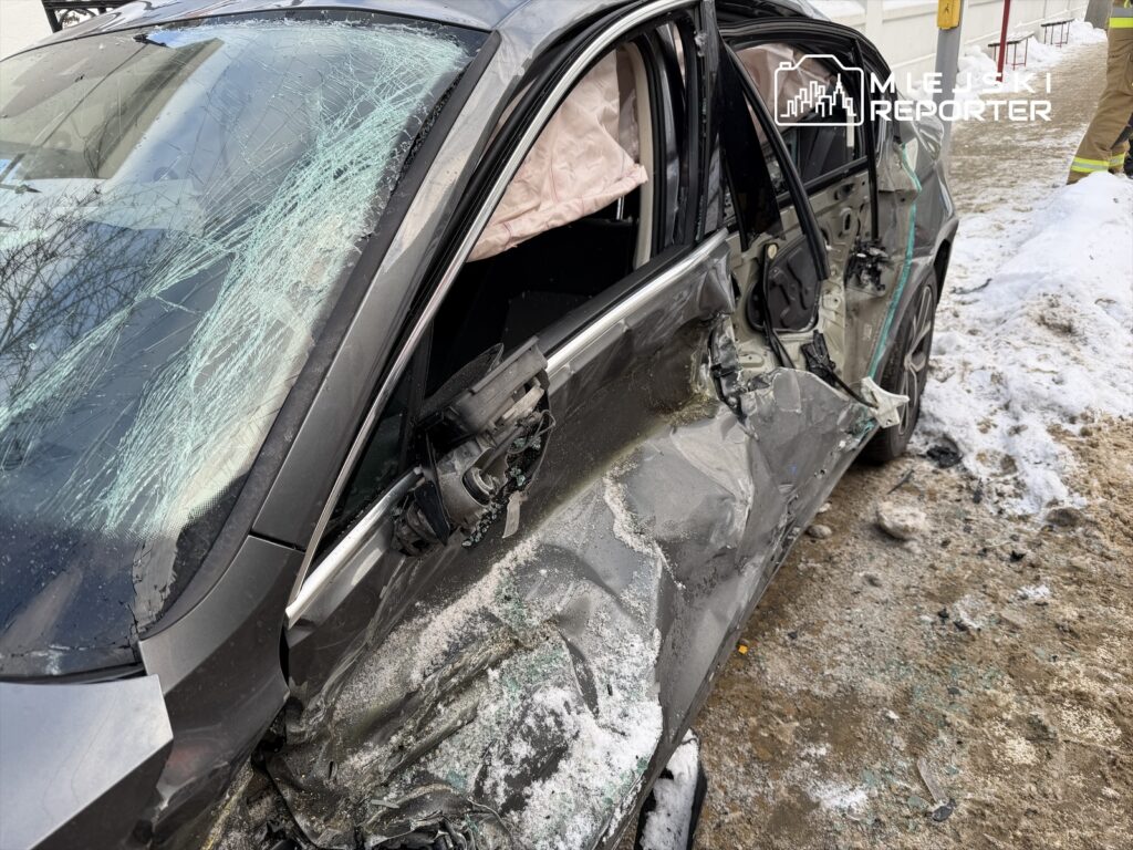 Uszkodzony samochód osobowy z wybitymi szybami stoi na zaśnieżonym chodniku, obok widać ślady po wypadku.