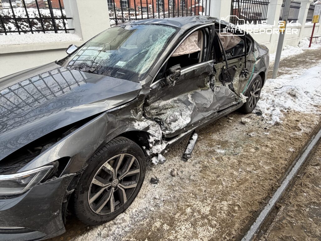 Uszkodzony samochód osobowy z wygiętą karoserią stoi na zaśnieżonym chodniku obok budynku.