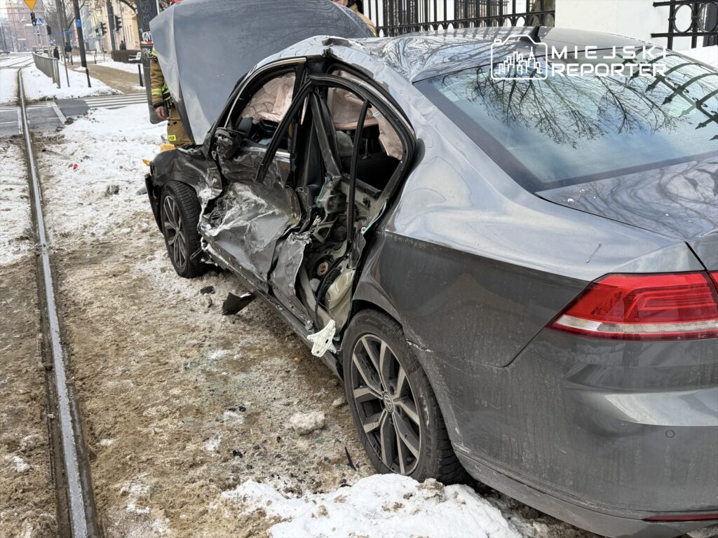 Uszkodzony samochód osobowy stoi na poboczu, z wyrwaną boczną częścią nadwozia, obok torów tramwajowych.