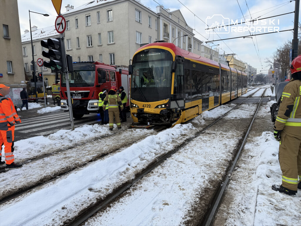 Strażacy i pracownicy służb ratunkowych pracują przy tramwaju na zaśnieżonej ulicy, obok stoi wóz strażacki.