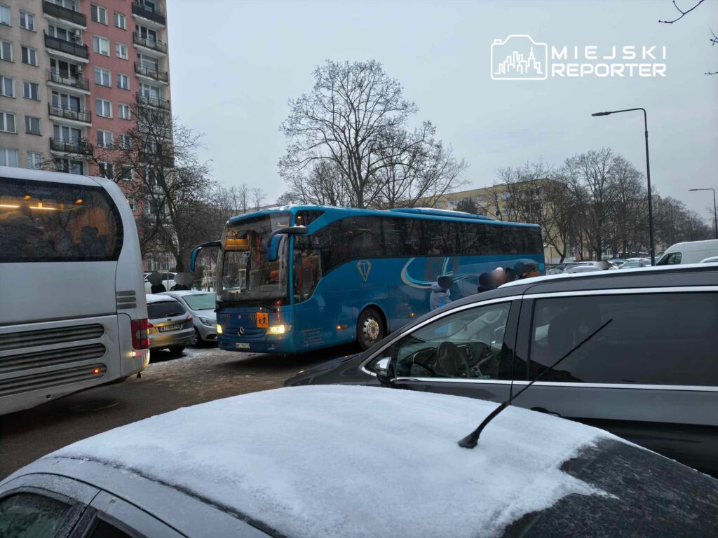 Autobus w niebieskim kolorze utknął w zatorze drogowym między zaparkowanymi samochodami w miejskiej okolicy.
