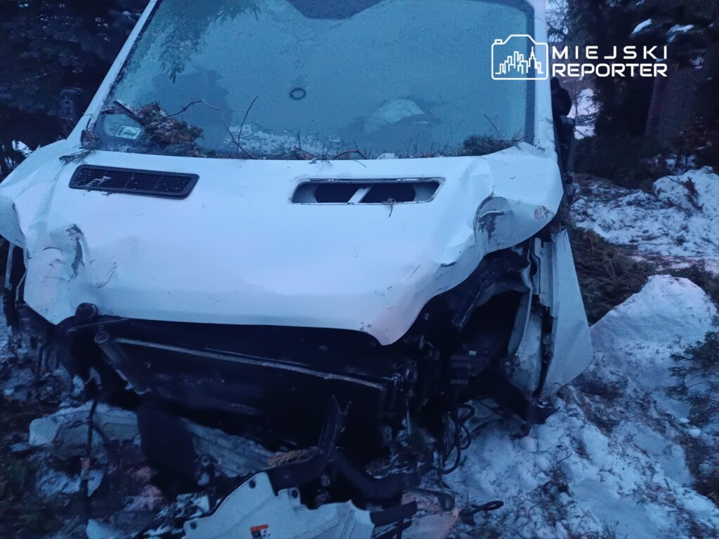 Uszkodzony biały pojazd leży na poboczu drogi, otoczony śniegiem i gałęziami drzew.