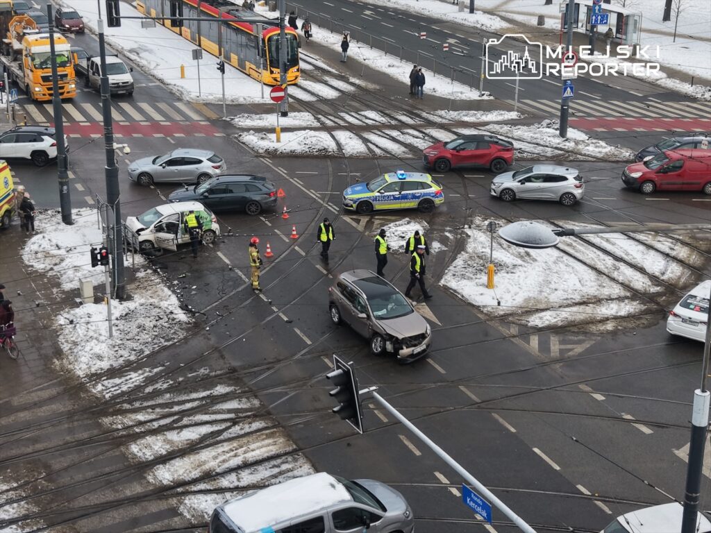 Na skrzyżowaniu z uszkodzonymi samochodami, policjanci i strażacy zabezpieczają miejsce wypadku.