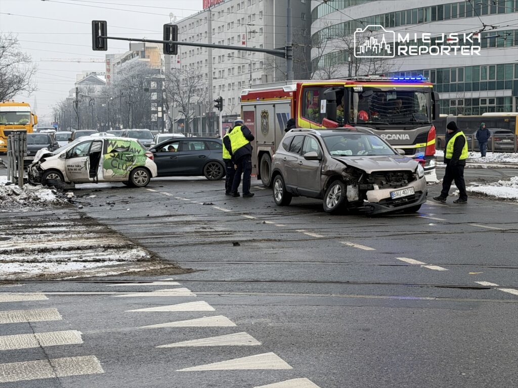 Dwa uszkodzone samochody po kolizji na skrzyżowaniu, obok wzywani ratownicy i straż pożarna w akcji.