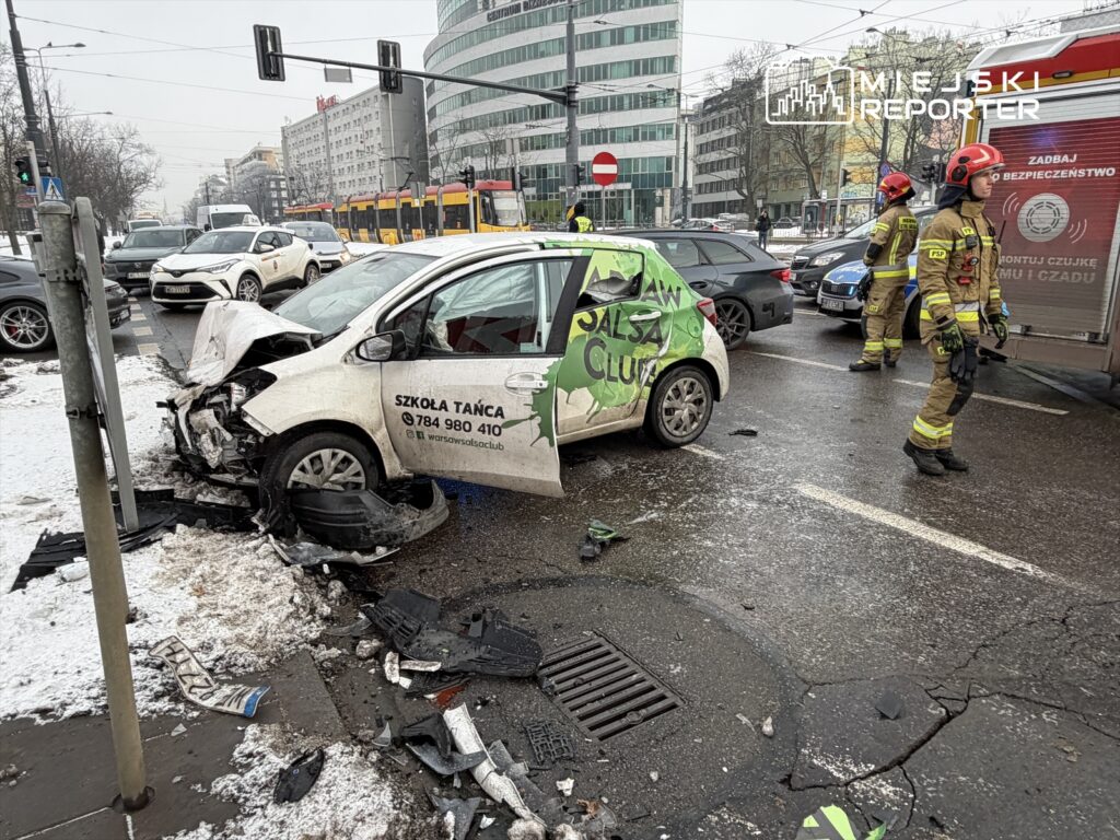 W wyniku wypadku drogowego uszkodzony samochód z logo szkoły tańca stoi na skrzyżowaniu, obok pracują strażacy.