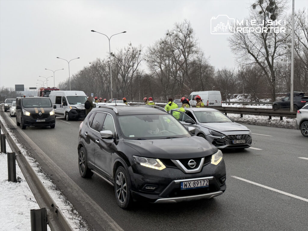 Grupa ratowników w żółtych kurtkach udziela pomocy na ruchliwej drodze, obok zablokowanych pojazdów.