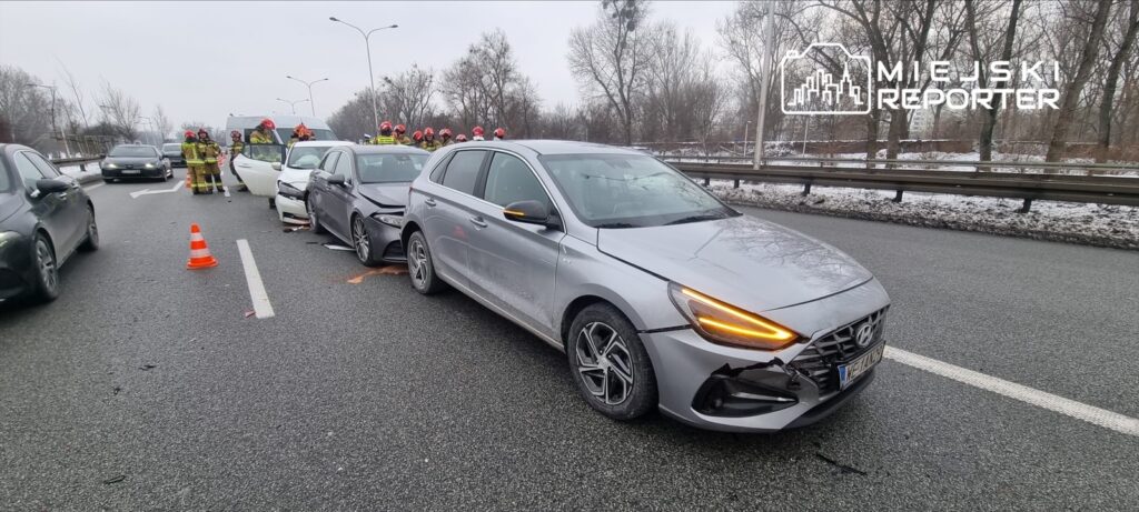 Wielu strażaków pracuje przy wypadku drogowym, w którym uczestniczy kilka uszkodzonych pojazdów na ruchliwej jezdni.