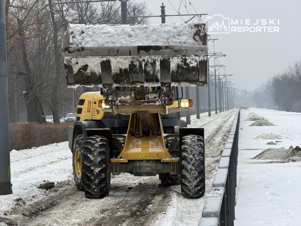 Maszyna do odśnieżania podnosi śnieg na zaśnieżonej drodze w miejskim otoczeniu.