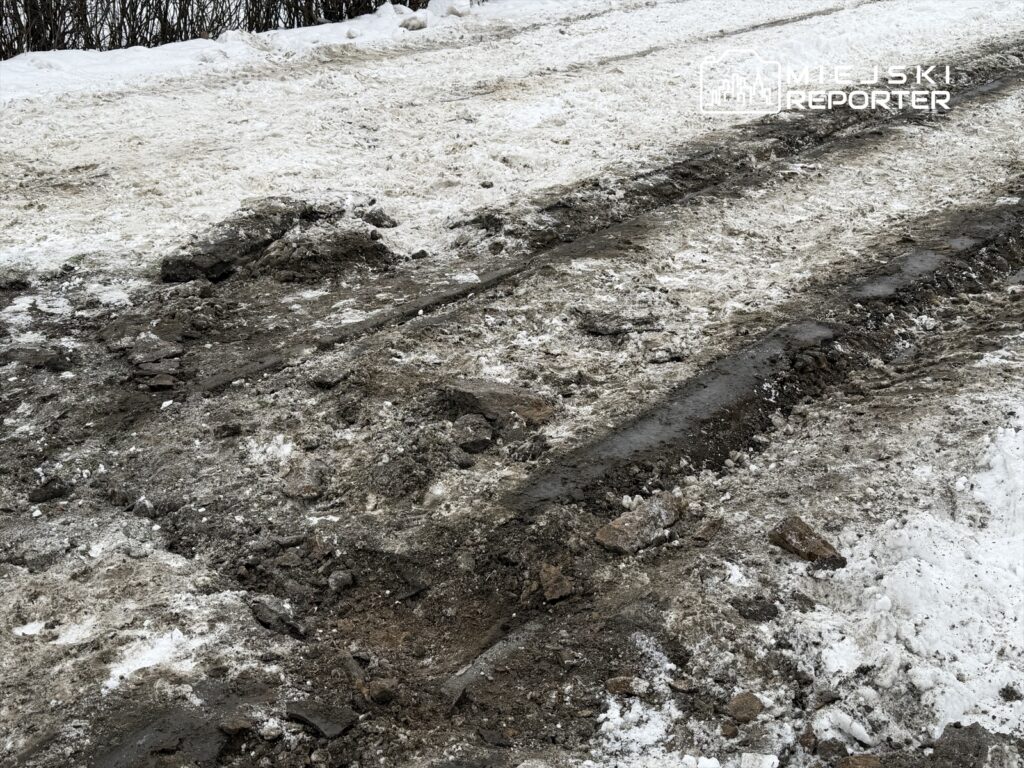 Zabrudzona droga z widocznymi śladami opon, pokryta resztkami śniegu i błota.