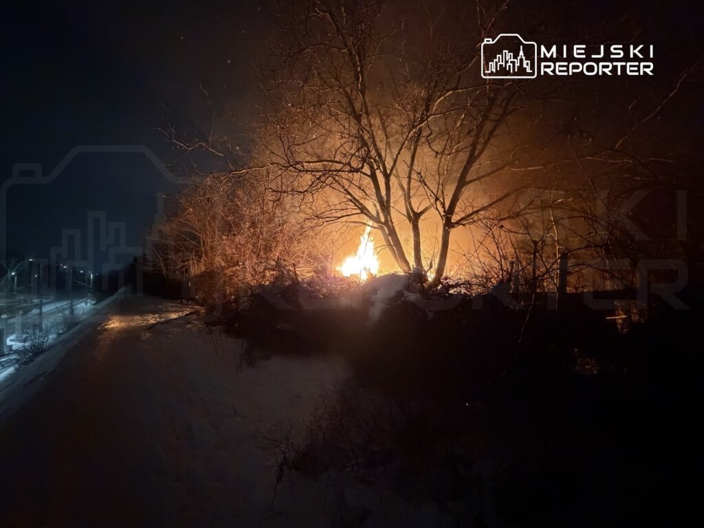 Ognisko płonące w zaroślach, w nocy, w pobliżu oświetlonej ścieżki.