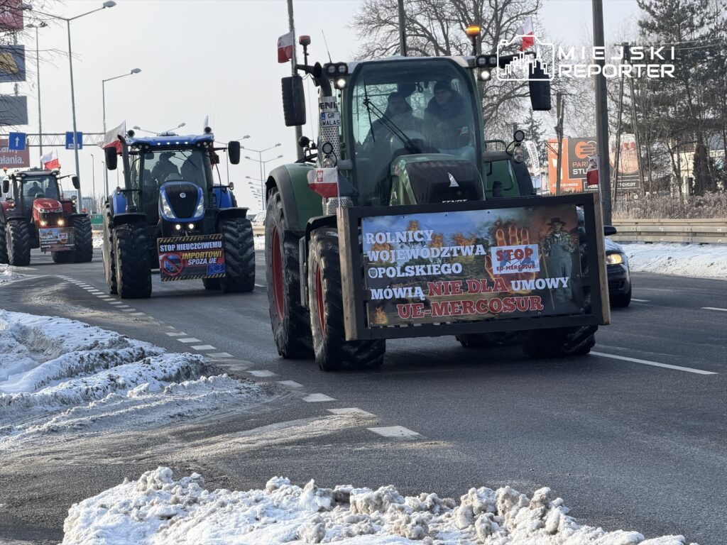 Traktory z transparentami przejeżdżają ulicą, protestując przeciw umowie UE-Mercosur. Na plakatach hasła: „STOP importowi spoza UE”.