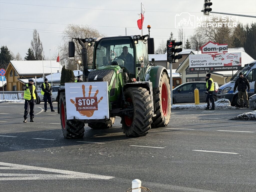 Traktor z napisem "STOP EU-MERCOSUR" stoi na skrzyżowaniu, a policjanci w żółtych kamizelkach kierują ruchem.