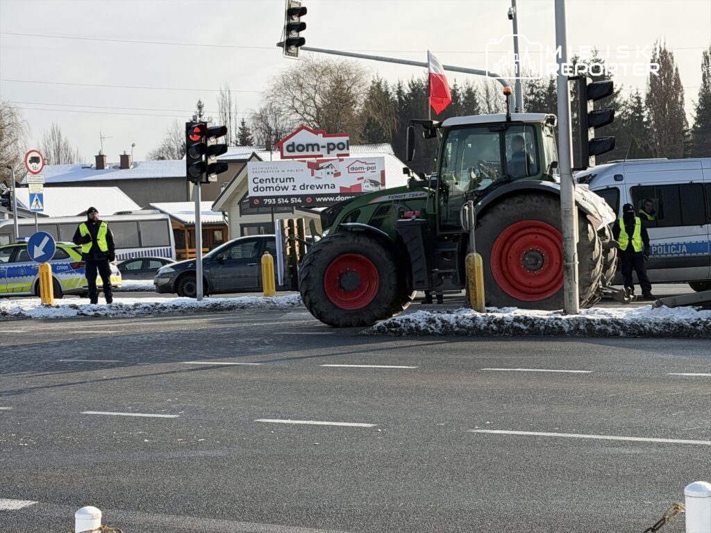 Traktor z flagą narodową zatrzymany na skrzyżowaniu, obok policjanci w kamizelkach odblaskowych.