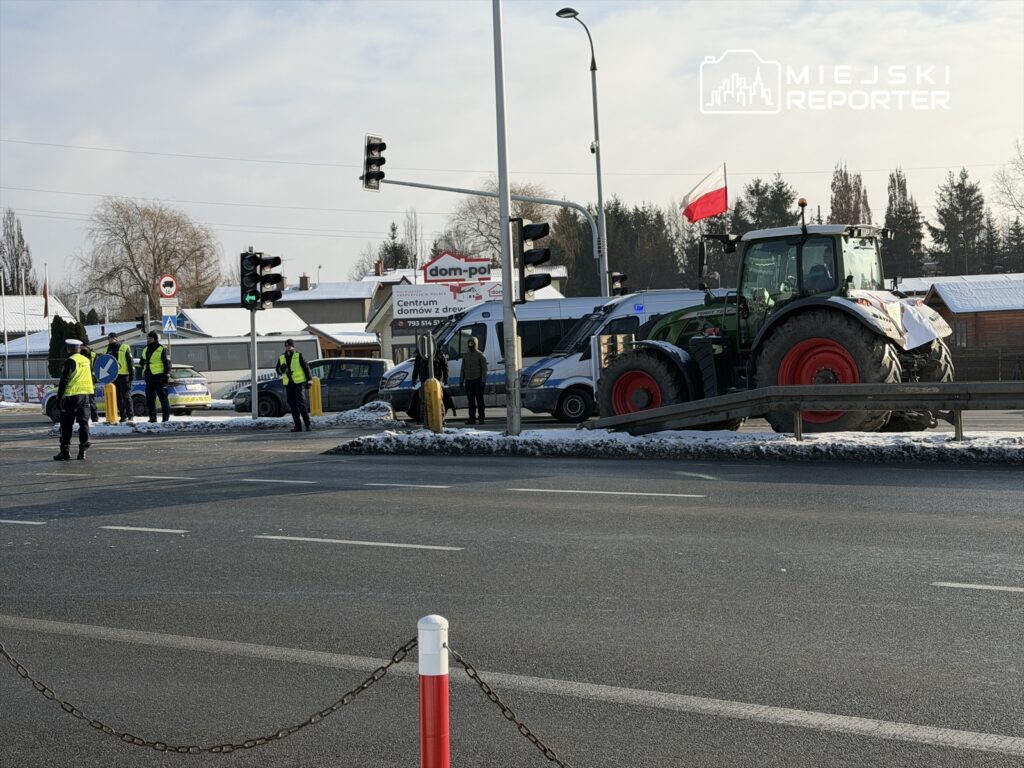Grupa policjantów w odblaskowych kamizelkach kieruje ruchem na skrzyżowaniu, obok stoi traktor z flagą.