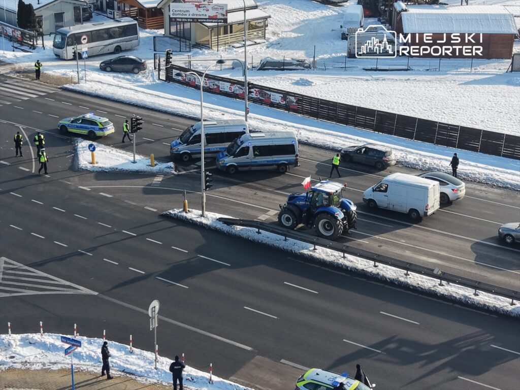 Traktor z flagą narodową stoi na drodze, a policjanci kierują ruchem w zaśnieżonym otoczeniu.