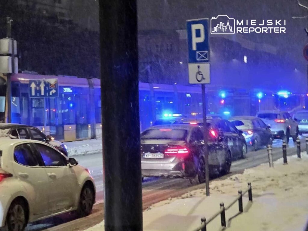 W nocy, w trakcie intensywnej śnieżycy, niebieskie światła sygnalizacyjne samochodów policyjnych odbijają się w śniegu na ulicy.