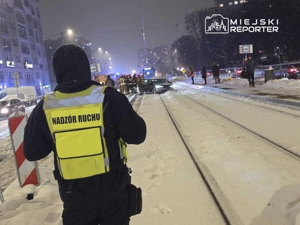 Funkcjonariusz w kamizelce "Nadzór Ruchu" obserwuje miejsce zdarzenia na zaśnieżonej ulicy, gdzie interweniują służby.