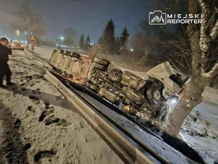 Cysterny leżąca na boku przy drodze, otoczona śniegiem i drzewami, a obok mężczyzna robiący zdjęcia.