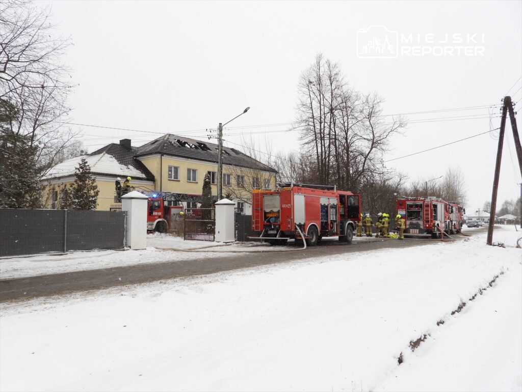 Strażacy pracują nad gaszeniem pożaru w budynku mieszkalnym, obok zaparkowane wozy strażackie w zimowej scenerii.