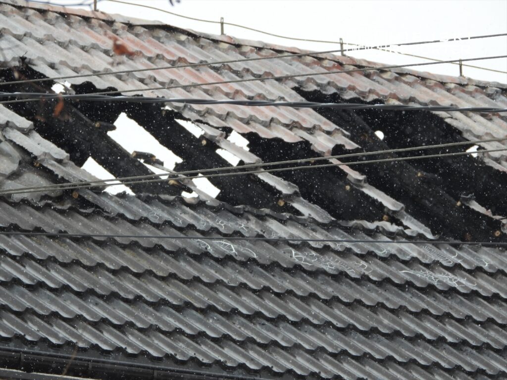 Część dachu z widocznymi uszkodzeniami i dziurami, przez które wpada śnieg, w otoczeniu przewodów elektrycznych.