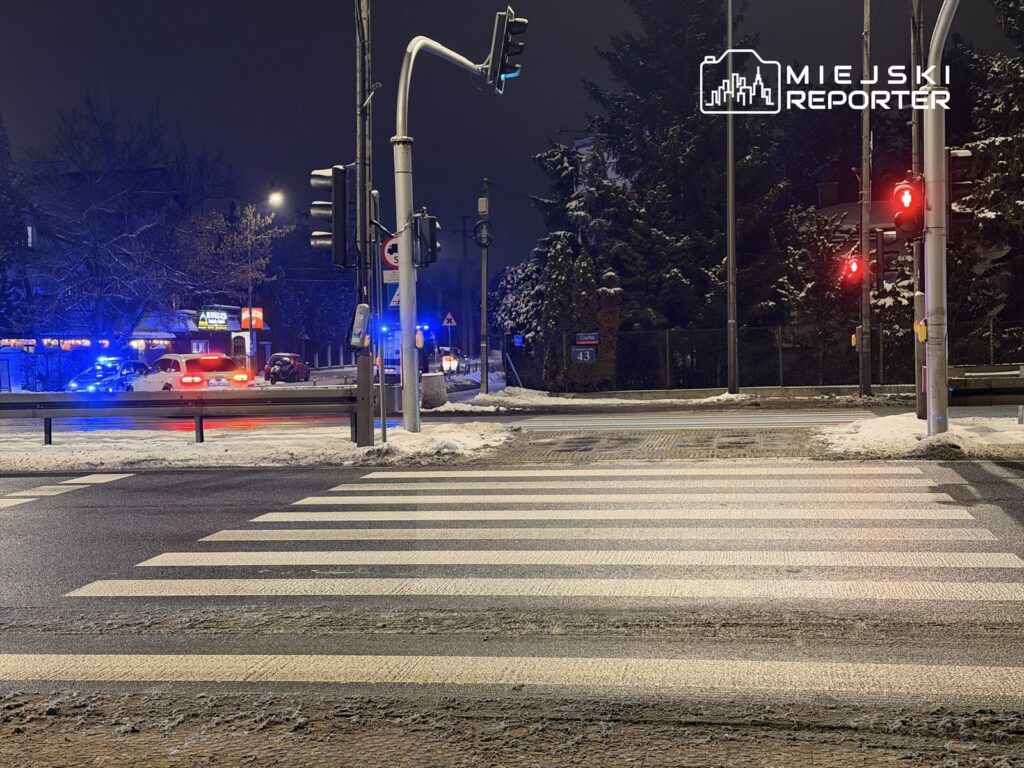 Policyjny radiowóz z włączonymi światłami błyskowymi zatrzymany przy przejściu dla pieszych na ośnieżonej ulicy.