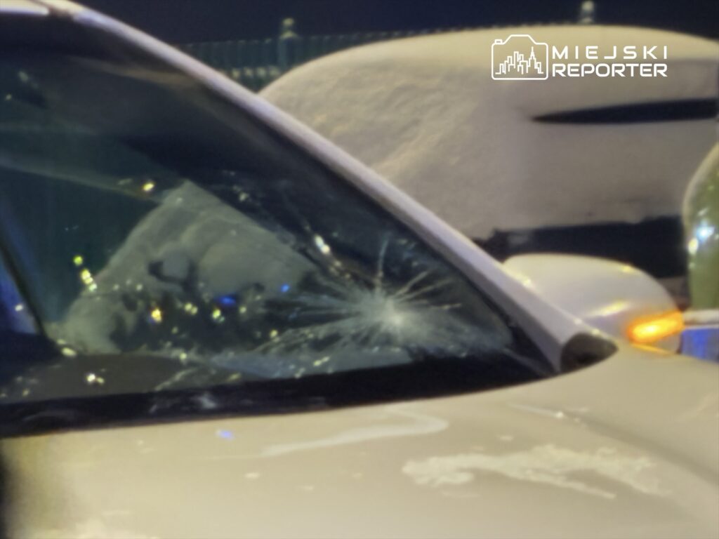 Pęknięta szyba samochodu zaparkowanego na ośnieżonym parkingu nocą.