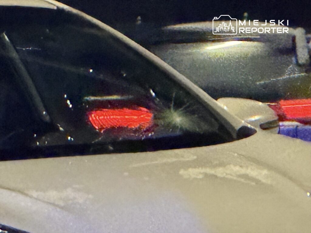 Zniszczona szyba samochodu z widoczną pękniętą powierzchnią oraz włączonymi światłami tylnymi.