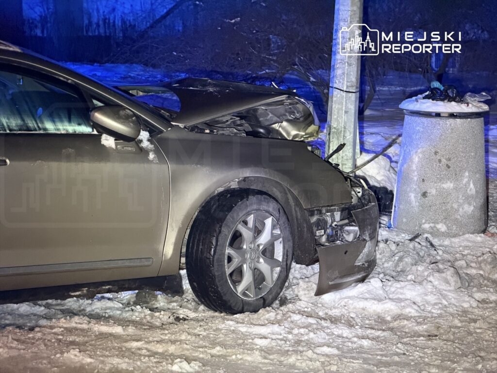 Zniszczony samochód osobowy uderzony w słup elektryczny na ośnieżonej drodze nocą.
