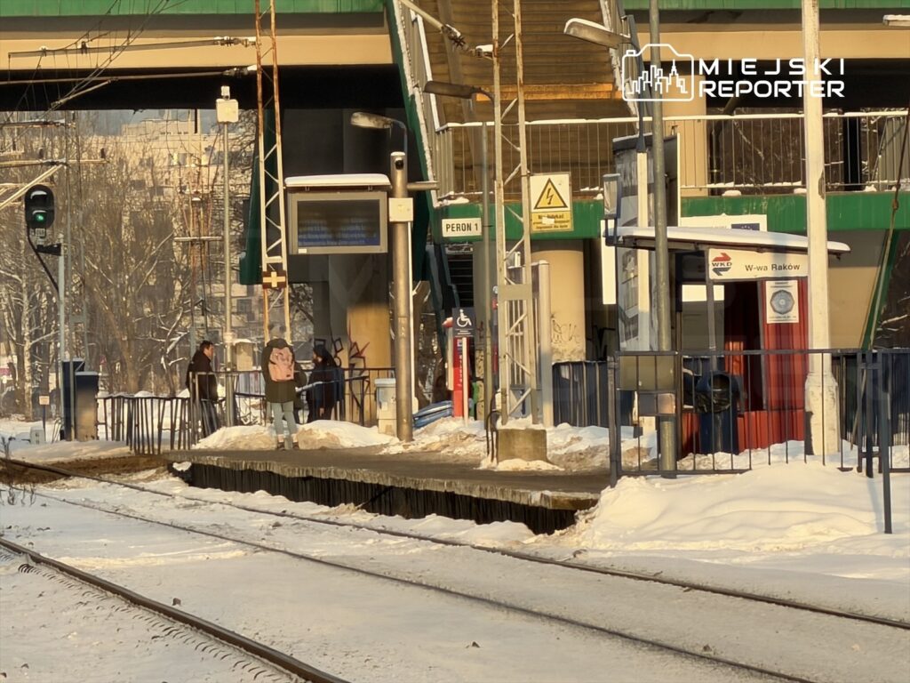 Pasażerowie czekają na peronie stacji kolejowej, otoczeni śniegiem i zimowym krajobrazem.