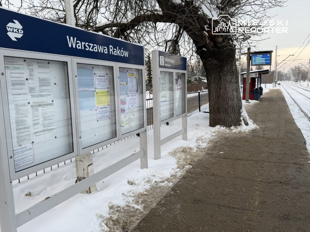Tablica ogłoszeń na przystanku Warszawa Raków, pokryta śniegiem, z widocznymi informacjami i rozkładami jazdy.