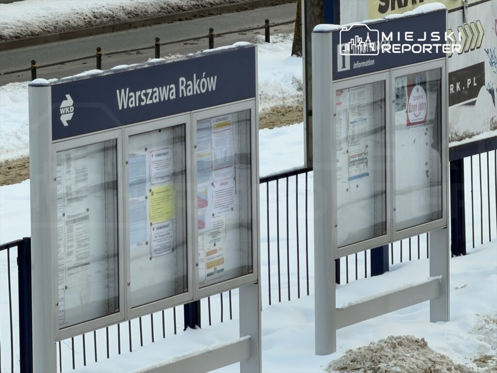 Tablica informacyjna z ogłoszeniami w zimowym otoczeniu, z napisem "Warszawa Raków" na górze.
