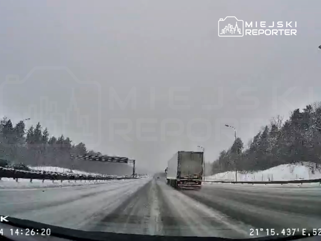 Ciężarówka porusza się po ośnieżonej autostradzie w zimowych warunkach, otoczona drzewami.