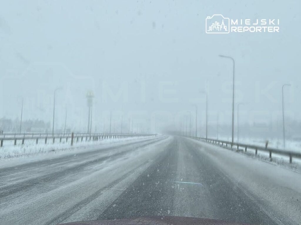 Droga pokryta śniegiem w trudnych warunkach atmosferycznych, widoczność ograniczona przez opady.