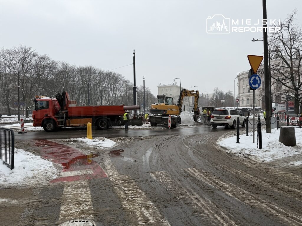 Wykonawcy prac budowlanych używają ciężkiego sprzętu na zaśnieżonej drodze w mieście.