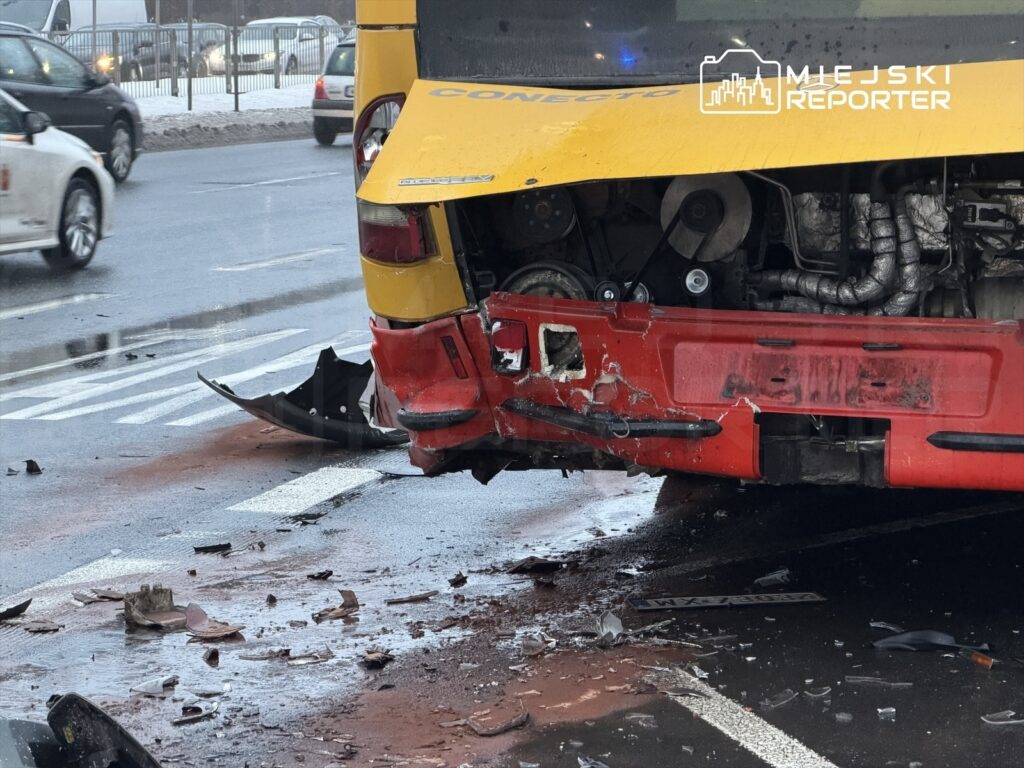Zniszczony autobus leży na jezdni, z uszkodzoną tylną częścią i odłamkami karoserii rozrzuconymi wokół.