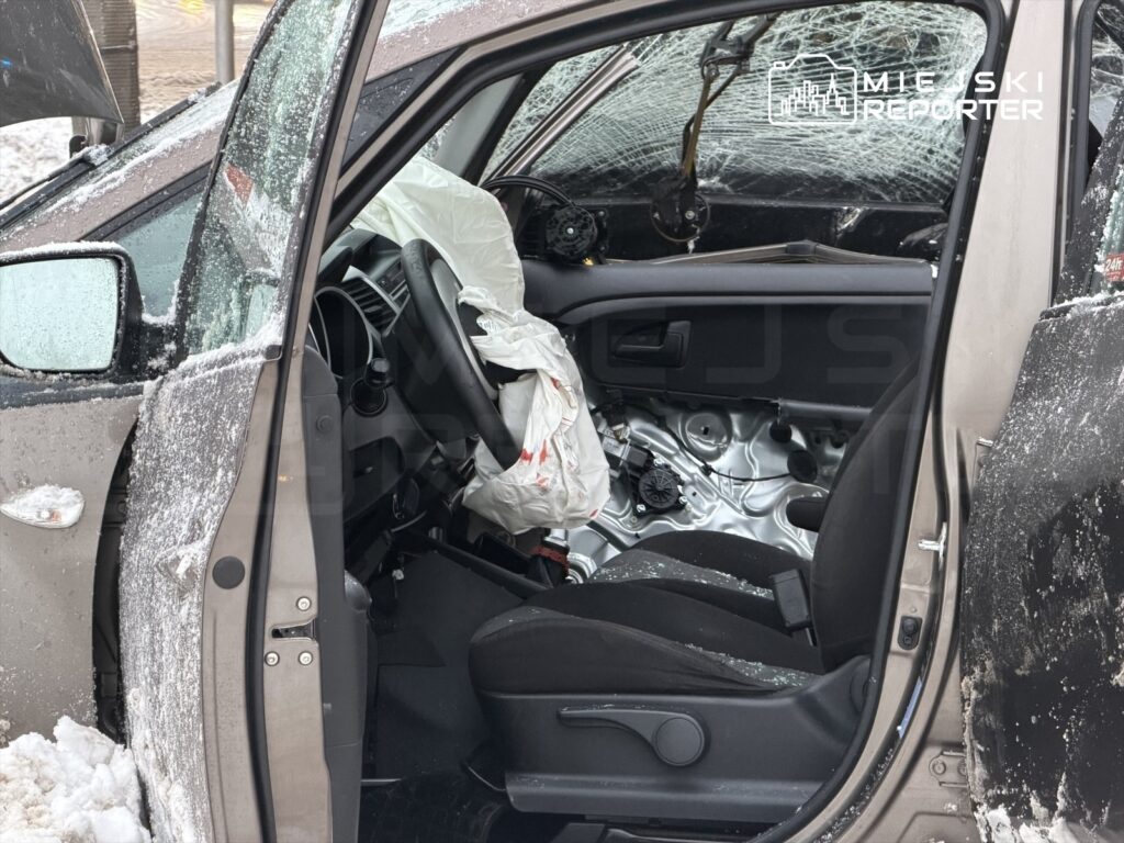 Uszkodzony samochód z wybitymi szybami stoi na śniegu, a poduszka powietrzna jest aktywowana w środku pojazdu.