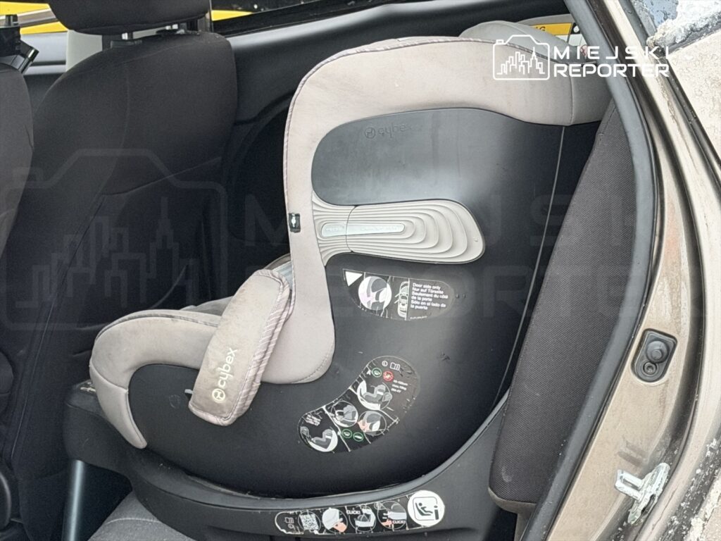 Fotelik samochodowy dla dziecka zamocowany na tylnym siedzeniu pojazdu. Widać instrukcje dotyczące montażu.