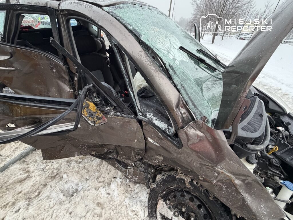 Uszkodzony samochód osobowy z wgniecioną stroną, stojący na zaśnieżonej drodze. Szyba przednia jest rozbita.