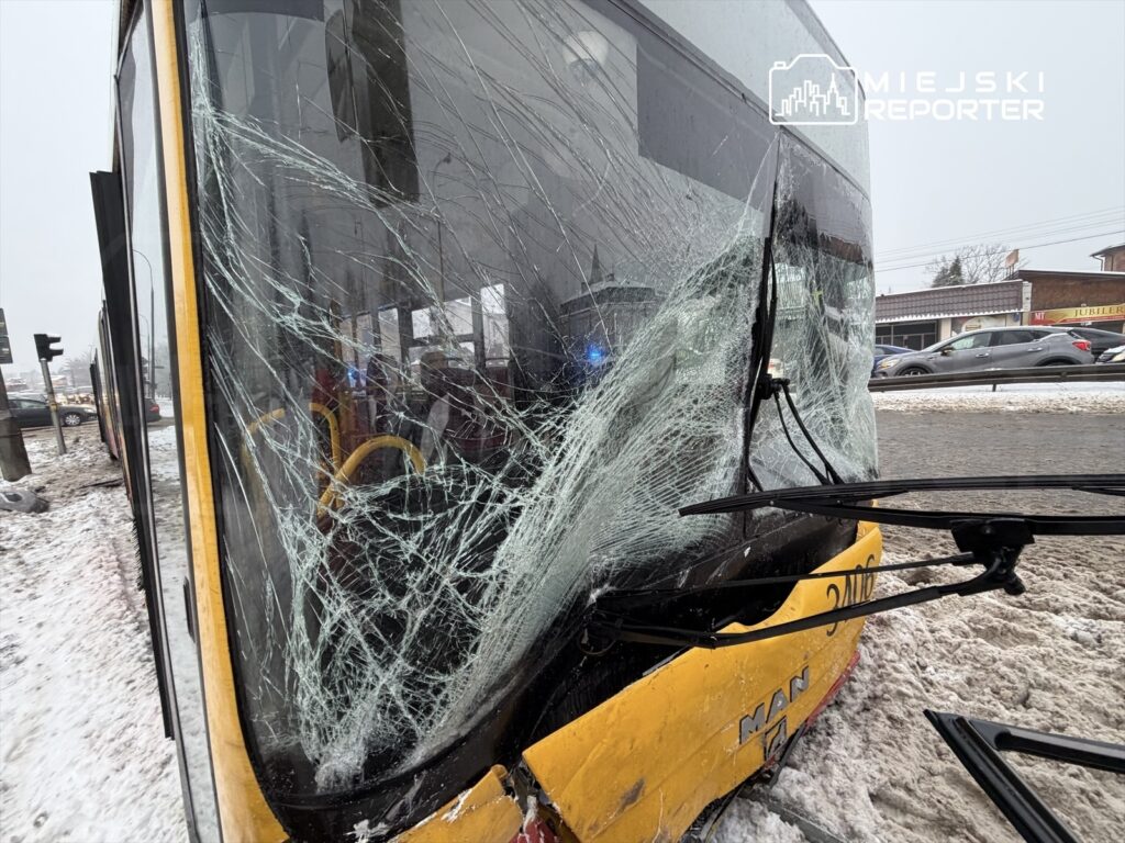 Uszkodzony tramwaj z pękniętą szybą przednią, zaparkowany na zaśnieżonej ulicy. W tle widoczne inne pojazdy i sygnalizacja świetlna.
