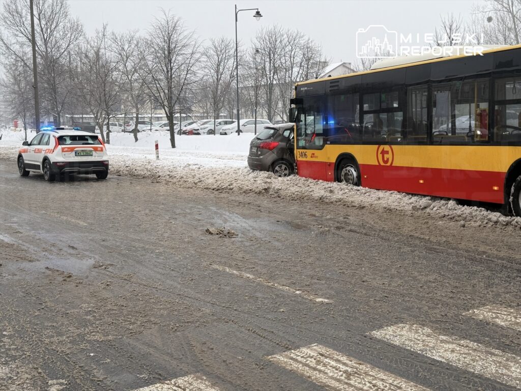 Policyjny radiowóz z włączonymi sygnałami świetlnymi stoi obok zatopionego w śniegu autobusu miejskiego na zaśnieżonej drodze.