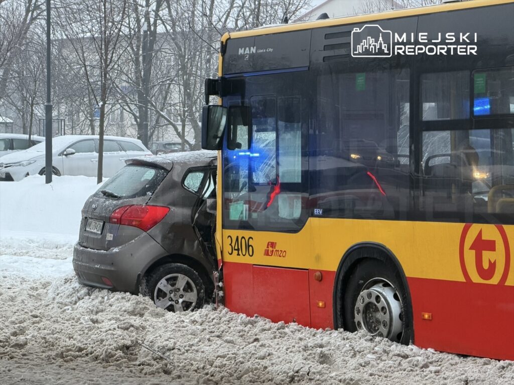 Zderzenie autobusu z osobowym samochodem na zaśnieżonej ulicy, oba pojazdy częściowo zakopane w śniegu.