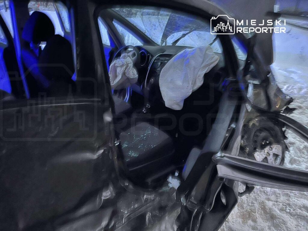 Wnętrze uszkodzonego samochodu osobowego z otwartymi drzwiami, w którym widać zainstalowaną poduszkę powietrzną i stłuczone szkło.