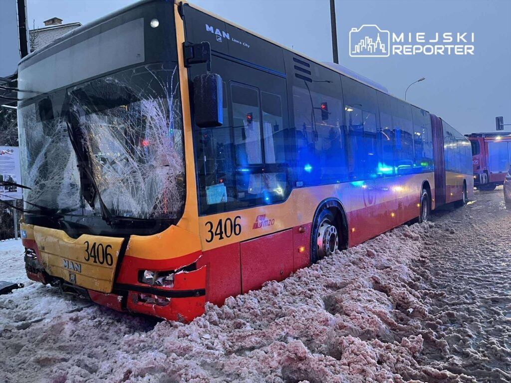Autobus z widocznymi uszkodzeniami przedniej szyby stoi w zasypanej śniegiem ulicy, obok widać pojazdy służb ratunkowych.