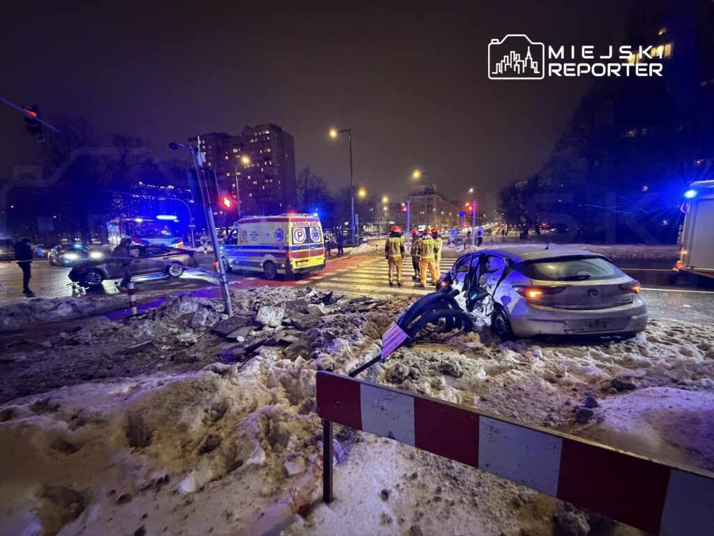 W nocy na ośnieżonym skrzyżowaniu pojazd osobowy uderzył w latarnię, a służby ratunkowe udzielają pomocy poszkodowanym.